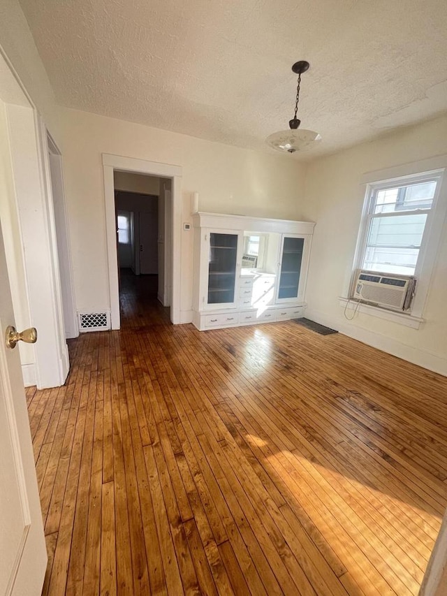 unfurnished living room with cooling unit, visible vents, wood-type flooring, and a textured ceiling