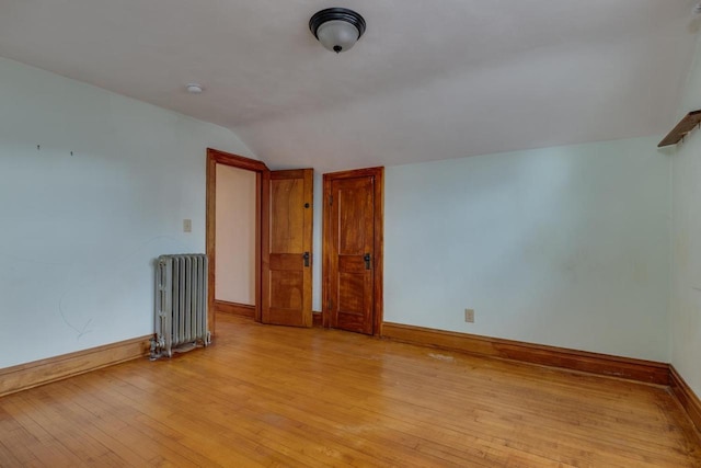 spare room with vaulted ceiling, radiator, baseboards, and light wood-type flooring