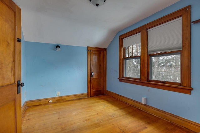 spare room featuring baseboards, light wood-style floors, and vaulted ceiling