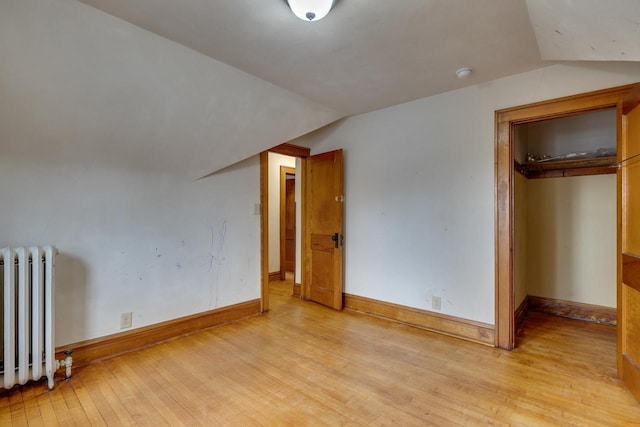 unfurnished bedroom featuring lofted ceiling, radiator, baseboards, and light wood finished floors