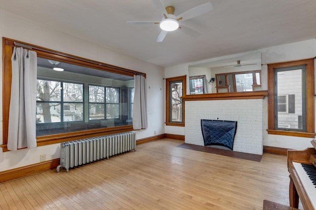 unfurnished living room with a ceiling fan, radiator heating unit, light wood finished floors, baseboards, and a brick fireplace