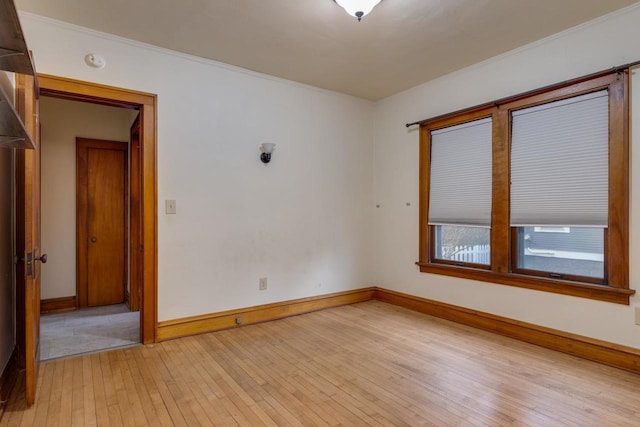 spare room featuring crown molding, light wood-type flooring, and baseboards