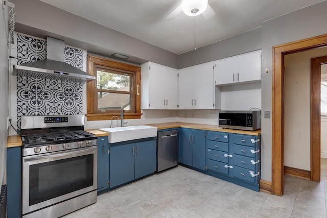 kitchen with blue cabinetry, wall chimney range hood, light countertops, stainless steel appliances, and a sink