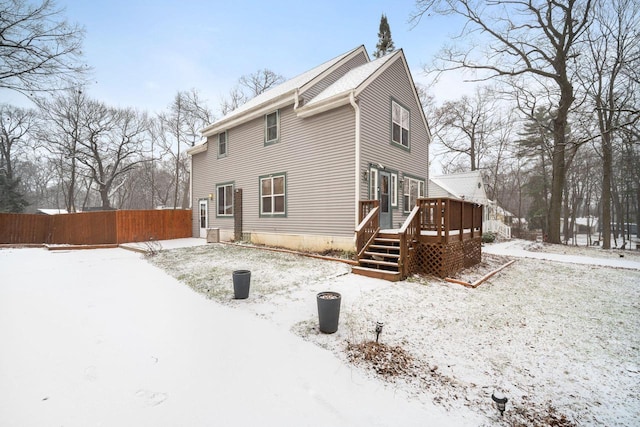 snow covered rear of property with fence and a wooden deck