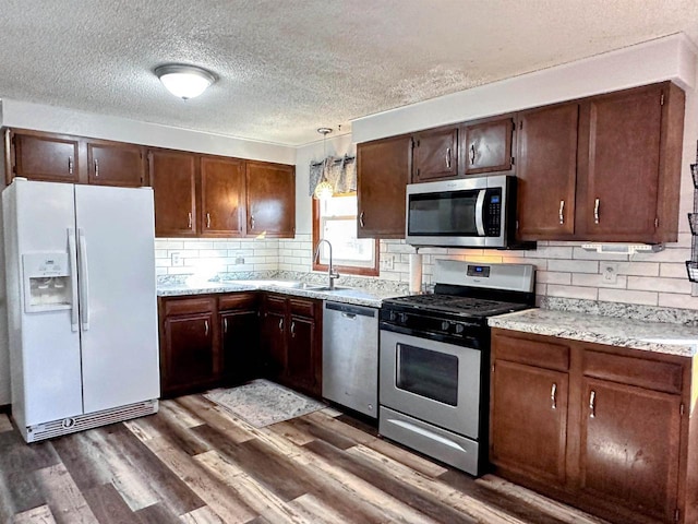 kitchen featuring dark wood finished floors, a sink, decorative backsplash, dark brown cabinetry, and appliances with stainless steel finishes