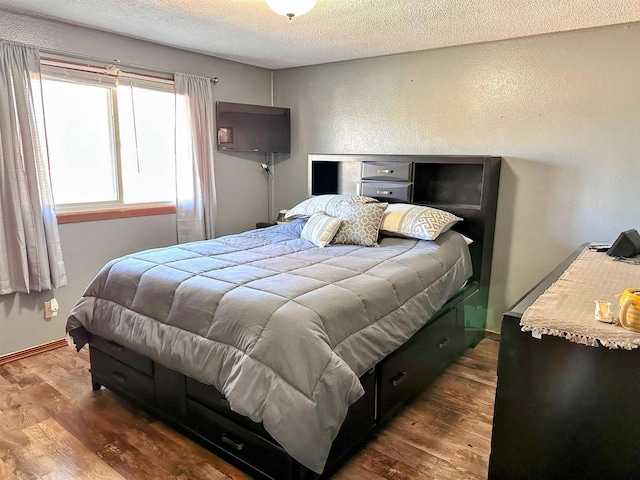 bedroom with a textured ceiling, baseboards, and wood finished floors