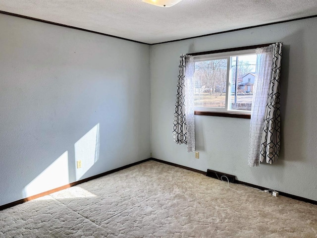 spare room with visible vents, a textured ceiling, carpet floors, baseboards, and a textured wall