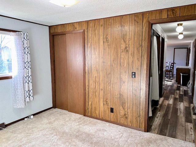 unfurnished bedroom with a closet, carpet floors, a textured ceiling, and wooden walls