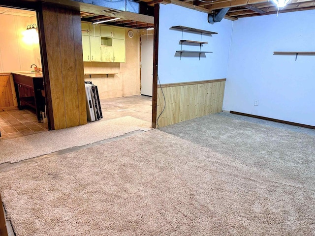 unfinished basement with carpet flooring, wood walls, and a sink