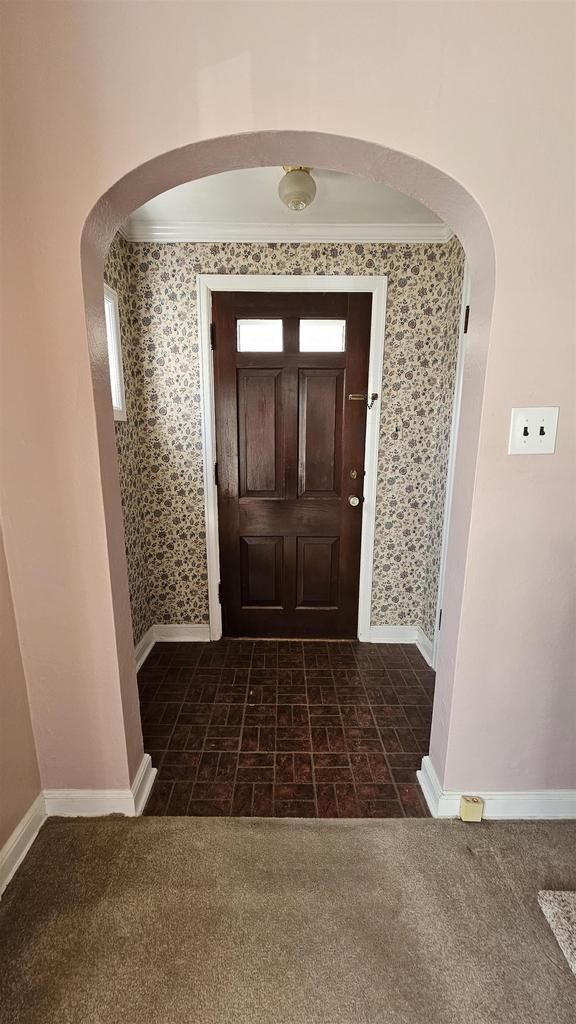 doorway with carpet flooring, baseboards, arched walkways, and ornamental molding