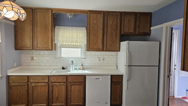 kitchen with a sink, white appliances, tasteful backsplash, and light countertops