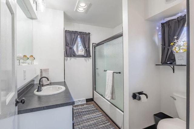 full bathroom with visible vents, vanity, toilet, and shower / bath combination with glass door