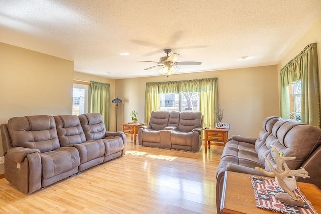 living room with a textured ceiling, a ceiling fan, and light wood-style floors