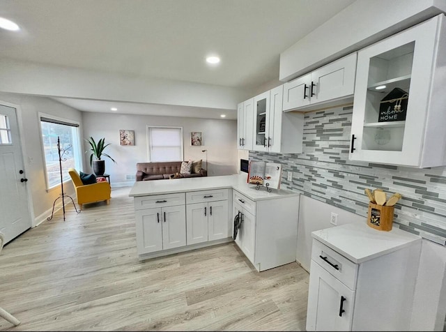 kitchen with backsplash, open floor plan, light countertops, light wood-style floors, and white cabinets