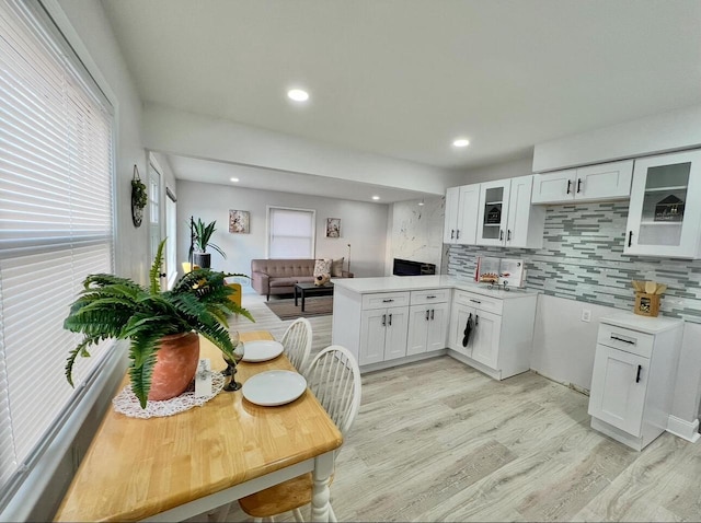 kitchen with a peninsula, white cabinets, glass insert cabinets, and light wood finished floors