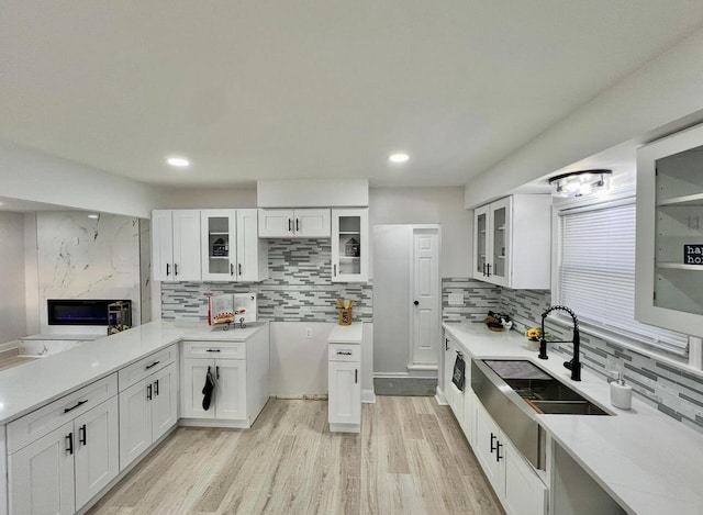 kitchen featuring a sink, light wood-type flooring, backsplash, and white cabinets