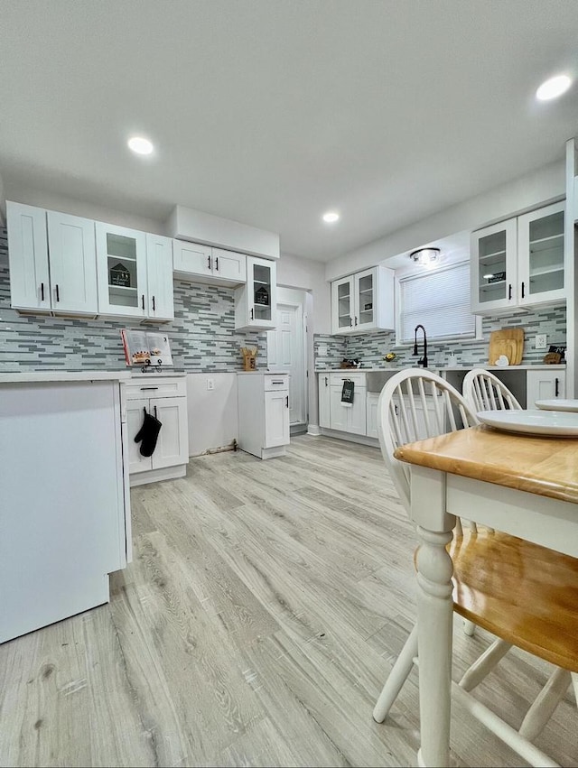 kitchen with light wood finished floors, tasteful backsplash, white cabinets, light countertops, and glass insert cabinets