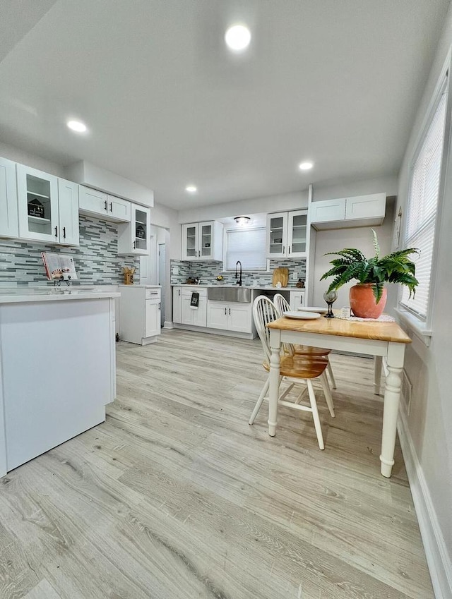 kitchen featuring a sink, white cabinets, glass insert cabinets, light wood-style floors, and tasteful backsplash