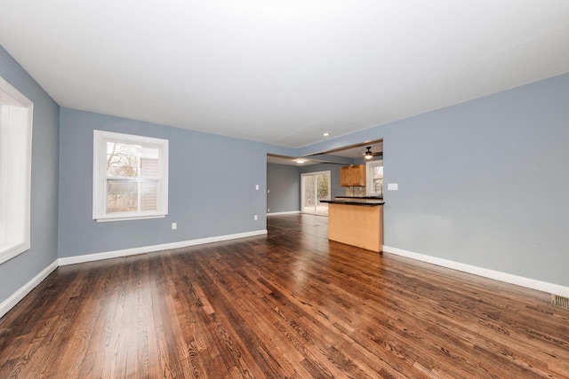 unfurnished living room with visible vents, baseboards, and dark wood-type flooring