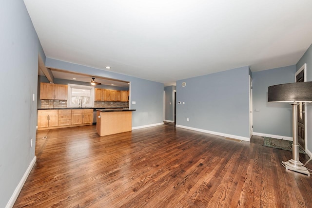 unfurnished living room with a sink, baseboards, and dark wood-style floors