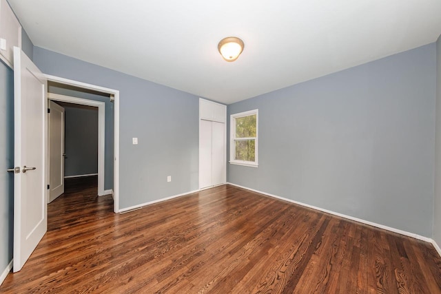 unfurnished bedroom with baseboards, dark wood-style flooring, and a closet