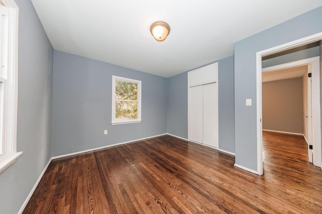 unfurnished bedroom featuring dark wood finished floors, baseboards, and a closet