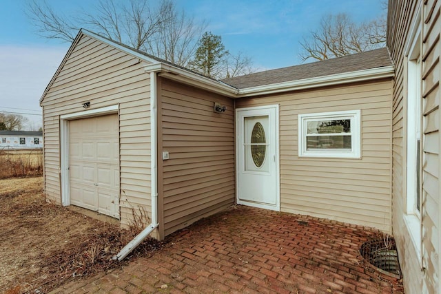 doorway to property with a garage and a shingled roof