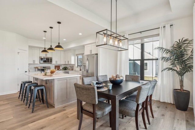 dining area with a raised ceiling, recessed lighting, baseboards, and light wood finished floors