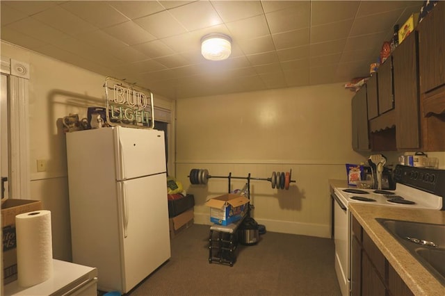 kitchen with dark brown cabinets, light countertops, wainscoting, white appliances, and a sink