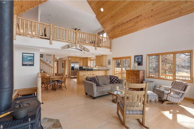 living area with light wood-type flooring, stairs, wooden ceiling, a wood stove, and high vaulted ceiling