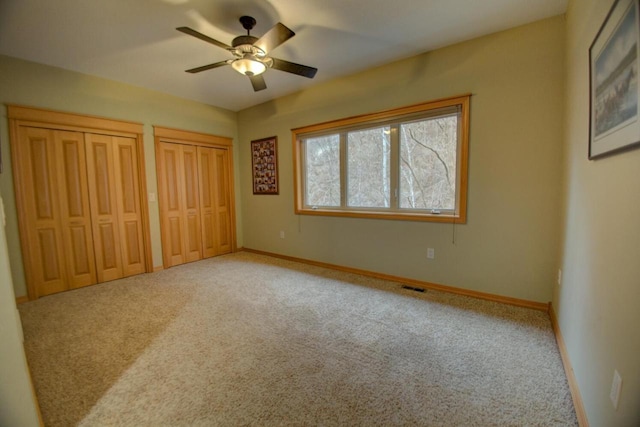 unfurnished bedroom with visible vents, carpet flooring, two closets, and baseboards