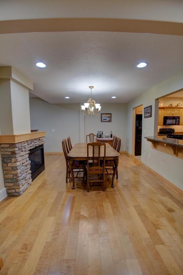 dining room with a chandelier, a stone fireplace, recessed lighting, and light wood-type flooring