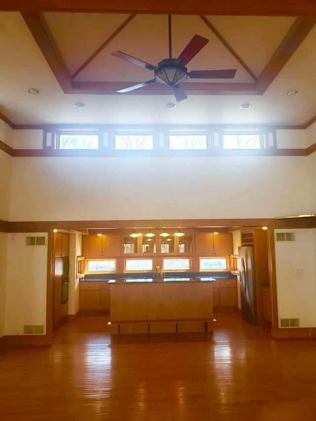 unfurnished living room with ceiling fan, visible vents, light wood-style floors, and a towering ceiling