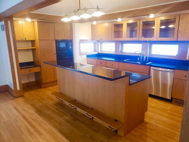 kitchen featuring light wood-style flooring, a sink, stainless steel dishwasher, dark countertops, and a center island