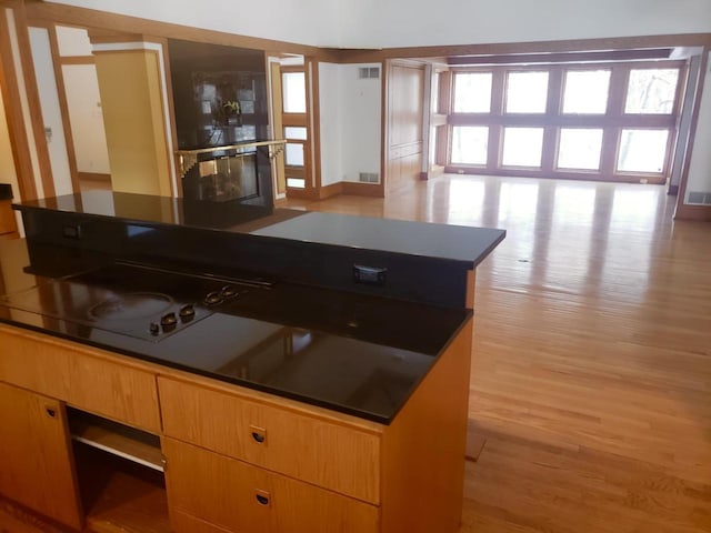 kitchen featuring visible vents, light wood-style floors, dark countertops, and a fireplace