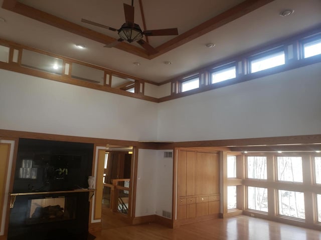 unfurnished living room featuring visible vents, a high ceiling, light wood-style flooring, and a ceiling fan