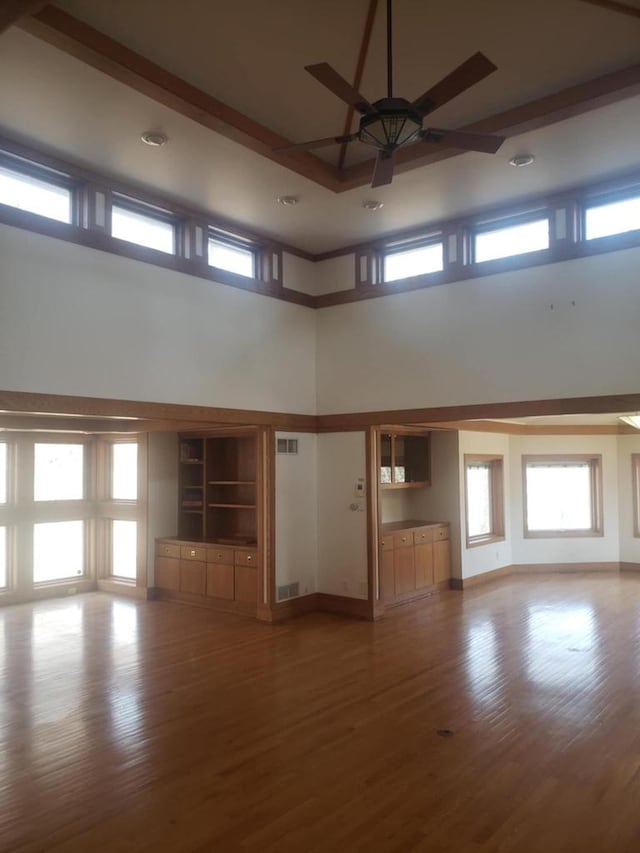 unfurnished living room featuring a wealth of natural light, wood finished floors, and a ceiling fan