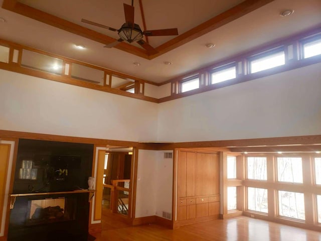 unfurnished living room with visible vents, ceiling fan, a towering ceiling, and light wood finished floors