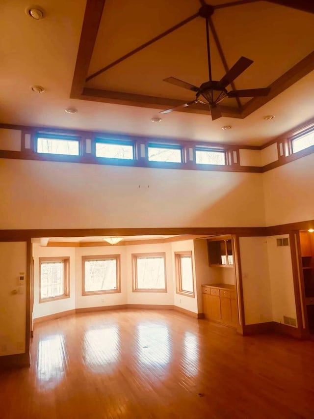 unfurnished living room featuring baseboards, a ceiling fan, a towering ceiling, and wood-type flooring