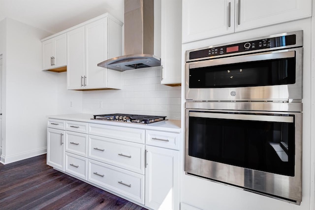 kitchen with wall chimney range hood, tasteful backsplash, dark wood finished floors, stainless steel appliances, and light countertops