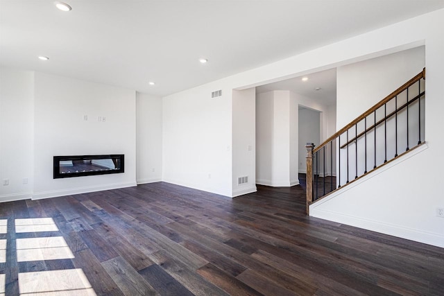 unfurnished living room with wood finished floors, visible vents, recessed lighting, stairs, and a glass covered fireplace