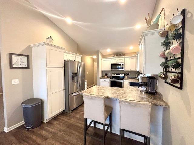 kitchen featuring dark wood finished floors, a peninsula, lofted ceiling, stainless steel appliances, and white cabinetry