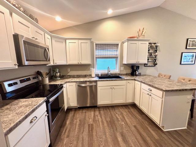 kitchen featuring a peninsula, stainless steel appliances, lofted ceiling, and a sink