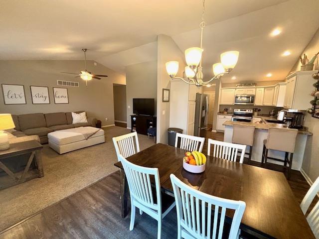 dining room with visible vents, baseboards, dark wood finished floors, vaulted ceiling, and ceiling fan with notable chandelier