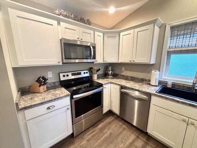 kitchen with dark wood-style flooring, a sink, stainless steel appliances, vaulted ceiling, and white cabinetry