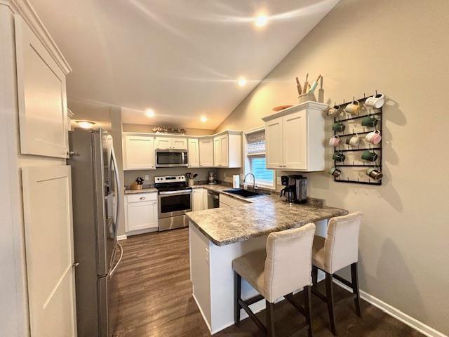 kitchen featuring a breakfast bar, a sink, appliances with stainless steel finishes, a peninsula, and vaulted ceiling