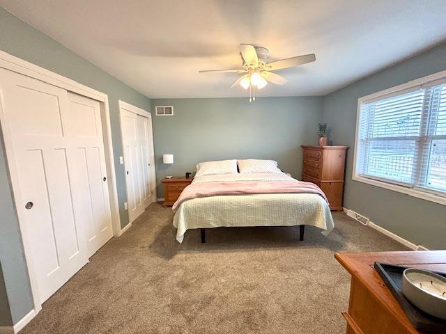 carpeted bedroom featuring visible vents, ceiling fan, baseboards, and multiple closets