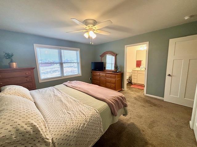 bedroom featuring ensuite bath, light colored carpet, baseboards, and ceiling fan