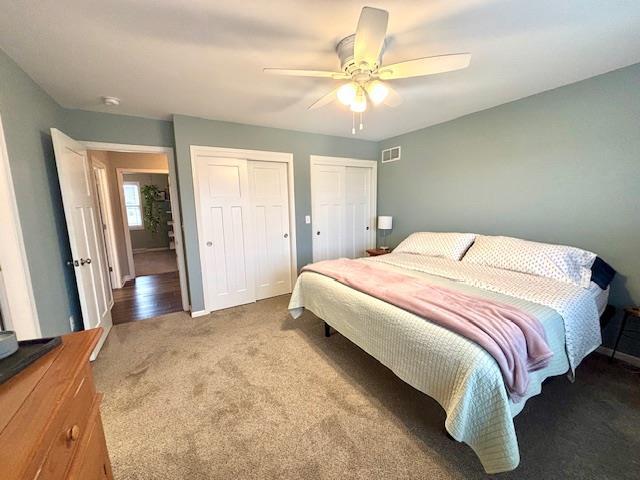 bedroom with carpet, visible vents, multiple closets, and ceiling fan