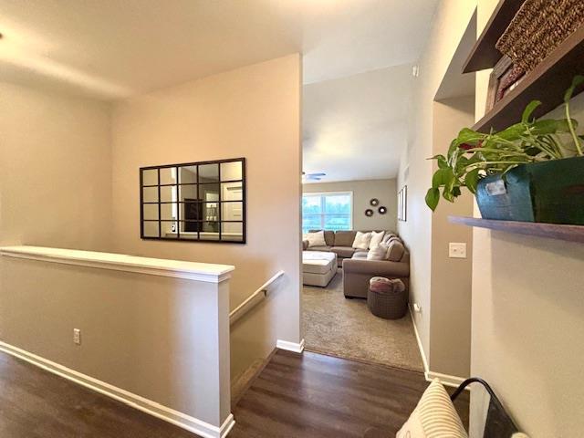 hallway with an upstairs landing, baseboards, and wood finished floors